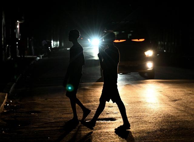 People cross a dark street during a blackout in Havana on March 4, 2026. (Photo by Yamil LAGE / AFP)