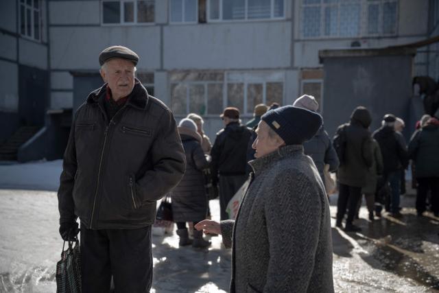 Grygory Gladysh (L), 79, the sole remaining resident of a heavily damaged 16-storey apartment building on the outskirts of Kharkiv, speak to a woman as their wait in line for hot meal distribution, on February 27, 2026, amid the Russian invasion of Ukraine. While millions of Ukrainians have been displaced internally or sought refuge abroad since the war began, many in dangerous areas are staying put, particularly elderly residents who lack the means or motivation to leave. (Photo by Ivan SAMOILOV / AFP)