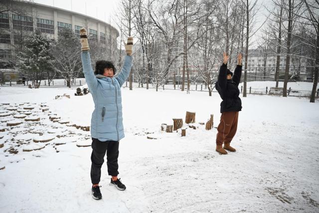 People excercise at park after an overnight snowfall in Beijing on March 5, 2026. (Photo by GREG BAKER / AFP)