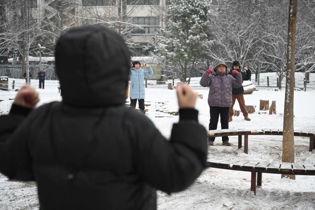 People excercise at park after an overnight snowfall in Beijing on March 5, 2026. (Photo by GREG BAKER / AFP)