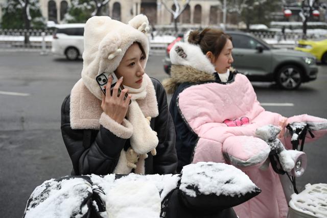 A woman makes a phone call while waiting on her scooter after an overnight snowfall in Beijing on March 5, 2026. (Photo by GREG BAKER / AFP)