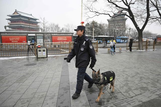 A police dog and its handler patrol on a street outside the Great Hall of the People, venue for the opening session of the National People's Congress (NPC), in Beijing on March 5, 2026. (Photo by Pedro PARDO / AFP)