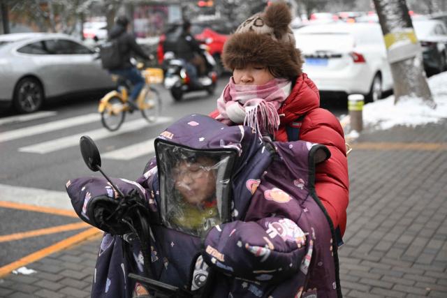 A woman rides a scooter as she carries a child along a street in Beijing on March 5, 2026. (Photo by Pedro PARDO / AFP)