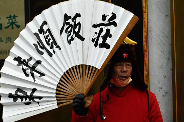 A man holds a fan as he promotes entry to the Donglaishun restaurant in Beijing on March 5, 2026. (Photo by Pedro PARDO / AFP)