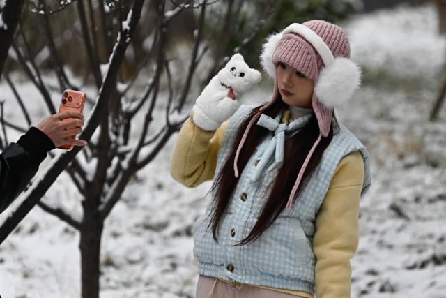 A woman poses for pictures in a park after an overnight snowfall in Beijing on March 5, 2026. (Photo by Pedro PARDO / AFP)