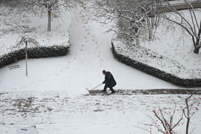 A worker clears snow from a path after an overnight snowfall in Beijing on March 5, 2026. (Photo by Pedro PARDO / AFP)
