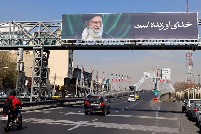 Motorists make their way along the road installed with a billboard of a picture of Iran's slain supreme leader Ayatollah Ali Khamenei, in Tehran on March 5, 2026. Iran announced that a state funeral for supreme leader Ayatollah Ali Khamenei, which had been planned for March 4 evening in Tehran, was postponed "in anticipation of unprecedented turnout," state television reported. (Photo by ATTA KENARE / AFP)