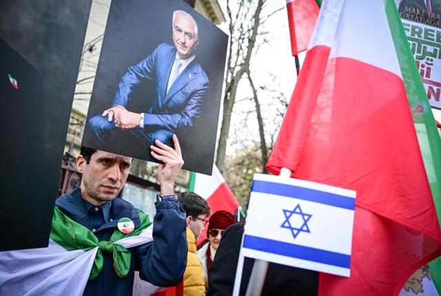 A member of the Iranian community to Romania holds holds a picture of  Iran's former crown prince and now key opposition figure Reza Pahlavi during a protest in front of the Iranian Embassy in Bucharest on March 5, 2026. Around one hundred participants held placards and chanted slogans in support of Israeli-US strikes on Iran and for the son of the last Shah of Iran, Reza Pahlavi, the most prominent figure in the Iranian opposition in exile. (Photo by Daniel MIHAILESCU / AFP)