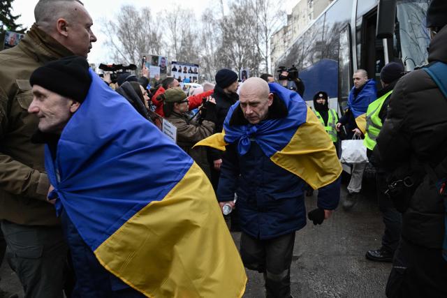 Released prisoners of war (POW) wrapped in a Ukrainian national flag walk past families holding portraits of their missing or captured relatives, upon their arrival following a prisoner exchange in the Chernygiv region on March 5, 2026, amid the Russian invasion of Ukraine. Ukraine and Russia each freed 200 prisoners of war, the first part of an exchange that will see them swap 500 people each in total, officials said. (Photo by Genya SAVILOV / AFP)