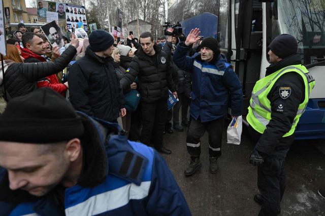 Released prisoners of war (POW) wrapped in a Ukrainian national flag walk past families holding portraits of their missing or captured relatives, upon their arrival following a prisoner exchange in the Chernygiv region on March 5, 2026, amid the Russian invasion of Ukraine. Ukraine and Russia each freed 200 prisoners of war, the first part of an exchange that will see them swap 500 people each in total, officials said. (Photo by Genya SAVILOV / AFP)