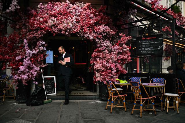 A waiter exits an entrance decorated with artificial flowers at a restaurant, in Paris, on March 5, 2026. (Photo by Julie SEBADELHA / AFP)