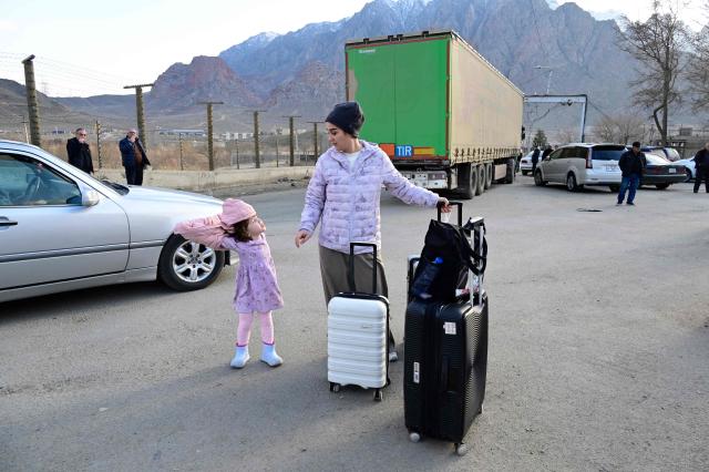 Iranian refugees stand next to luggage after crossing the border from Iran to Armenia at a border check point in the southern Armenian town of Gyumri, on March 5, 2026, amid the Middle East war. The United States and Israel began a sweeping military campaign against Iran, targeting missile facilities, naval assets and other infrastructure, with strikes triggering retaliatory attacks across the region. (Photo by KAREN MINASYAN / AFP)