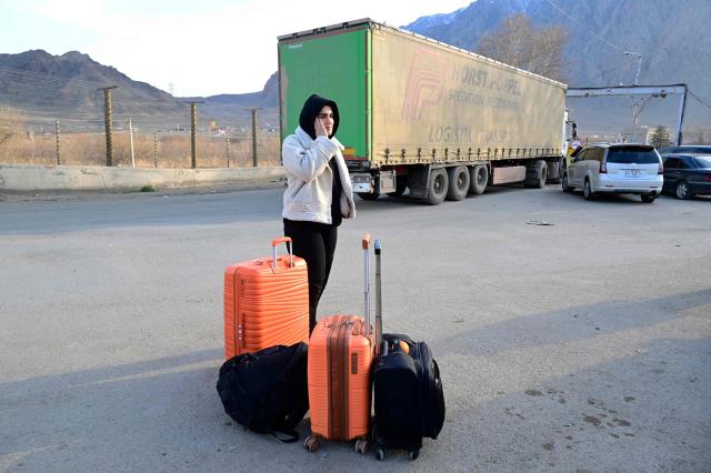 An Iranian refugee stands next to luggage and holds a smartphone after crossing the border from Iran to Armenia at a border check point in the southern Armenian town of Gyumri, on March 5, 2026, amid the Middle East war. The United States and Israel began a sweeping military campaign against Iran, targeting missile facilities, naval assets and other infrastructure, with strikes triggering retaliatory attacks across the region. (Photo by KAREN MINASYAN / AFP)