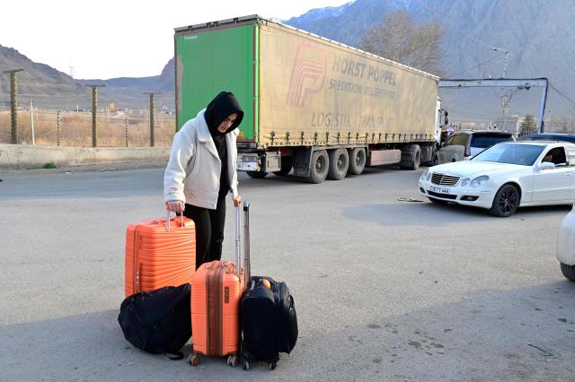 An Iranian refugee stands next to luggage after crossing the border from Iran to Armenia at a border check point in the southern Armenian town of Gyumri, on March 5, 2026, amid the Middle East war. The United States and Israel began a sweeping military campaign against Iran, targeting missile facilities, naval assets and other infrastructure, with strikes triggering retaliatory attacks across the region. (Photo by KAREN MINASYAN / AFP)