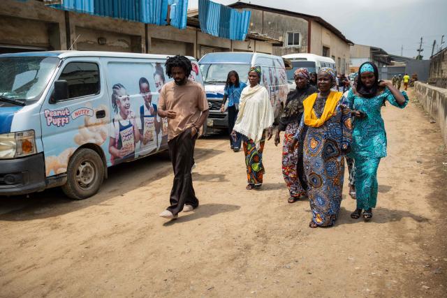 Kachi Benson (L), the director of the documentary Mothers of Chibok, walks alongside the women during a visit to the Nutzy peanut butter factory in Lagos on February 27, 2026. Nine women from Chibok are collaborating with Zenfix Nigeria, a company that sells peanuts and nut products, and Arjena Foods, producer of the Nutzy peanut butter brand, which is very popular in Nigeria. 
This partnership was supported by Joel Kachi Benson, director of the documentary "Mothers of Chibok," released in theaters last week, which chronicles the lives of these mothers. 
Before the creation of Mothers of Chibok, their harvests were sold unprocessed to middlemen in the village, generating meager and unpredictable incomes. Today, they work has better value, they obtain a stable income, and reach a wider audience. 
These women's peanut production increased from 15 100kg bags to 27 bags between 2024 and 2025.
For Ajrena Foods and Zenfix Nigeria, the initiative is part of a social and economic reconstruction project that could inspire other mothers whose children have also been abducted by Boko Haram, other jihadist groups, or criminal gangs. (Photo by TOYIN ADEDOKUN / AFP)