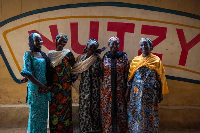 The mothers pose for a group photo inside the factory during their visit to the processing company in Lagos on February 27, 2026. Nine women from Chibok are collaborating with Zenfix Nigeria, a company that sells peanuts and nut products, and Arjena Foods, producer of the Nutzy peanut butter brand, which is very popular in Nigeria. 
This partnership was supported by Joel Kachi Benson, director of the documentary "Mothers of Chibok," released in theaters last week, which chronicles the lives of these mothers. 
Before the creation of Mothers of Chibok, their harvests were sold unprocessed to middlemen in the village, generating meager and unpredictable incomes. Today, they work has better value, they obtain a stable income, and reach a wider audience. 
These women's peanut production increased from 15 100kg bags to 27 bags between 2024 and 2025.
For Ajrena Foods and Zenfix Nigeria, the initiative is part of a social and economic reconstruction project that could inspire other mothers whose children have also been abducted by Boko Haram, other jihadist groups, or criminal gangs. (Photo by TOYIN ADEDOKUN / AFP)