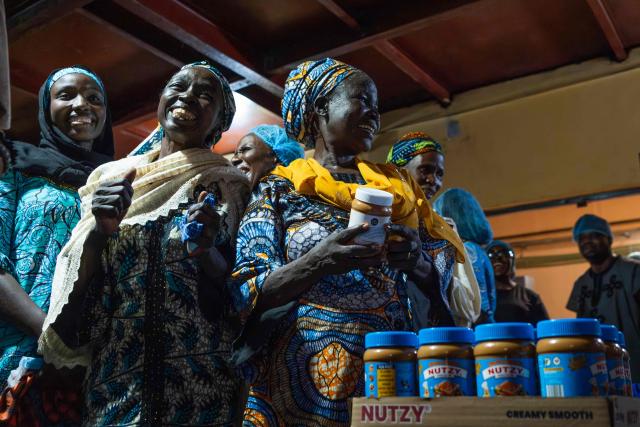 Yana Galang, 55, reacts as she holds a packaged Nutzy Peanut Butter during their visit to the factory in Lagos on February 27, 2026. Nine women from Chibok are collaborating with Zenfix Nigeria, a company that sells peanuts and nut products, and Arjena Foods, producer of the Nutzy peanut butter brand, which is very popular in Nigeria. 
This partnership was supported by Joel Kachi Benson, director of the documentary "Mothers of Chibok," released in theaters last week, which chronicles the lives of these mothers. 
Before the creation of Mothers of Chibok, their harvests were sold unprocessed to middlemen in the village, generating meager and unpredictable incomes. Today, they work has better value, they obtain a stable income, and reach a wider audience. 
These women's peanut production increased from 15 100kg bags to 27 bags between 2024 and 2025.
For Ajrena Foods and Zenfix Nigeria, the initiative is part of a social and economic reconstruction project that could inspire other mothers whose children have also been abducted by Boko Haram, other jihadist groups, or criminal gangs. (Photo by TOYIN ADEDOKUN / AFP)