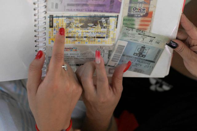 America de Cali's fans Jessica Avila and Angelica Ariza from the Colectivo Futbolero Escarlata look at old football match tickets before attending the Copa Sudamericana football match between Colombia's America de Cali and Atletico Bucaramanga at the Olimpico Pascual Guerrero Stadium in Cali, Colombia on March 5, 2026. With a drum, a female fan sets the pace for the chants of a feminist fan club at the stadium in the Colombian city of Manizales. "One, two, three!" she says like an orchestra conductor surrounded exclusively by women tired of machismo in football, as is the case in other countries such as Brazil. (Photo by JOAQUIN SARMIENTO / AFP)