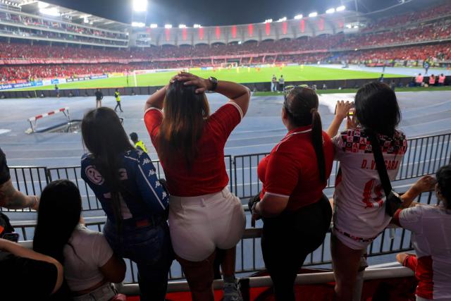 America de Cali's fans from the Colectivo Futbolero Escarlata cheer for their team during the Copa Sudamericana football match between Colombia's America de Cali and Atletico Bucaramanga at the Olimpico Pascual Guerrero Stadium in Cali, Colombia on March 5, 2026. With a drum, a female fan sets the pace for the chants of a feminist fan club at the stadium in the Colombian city of Manizales. "One, two, three!" she says like an orchestra conductor surrounded exclusively by women tired of machismo in football, as is the case in other countries such as Brazil. (Photo by JOAQUIN SARMIENTO / AFP)