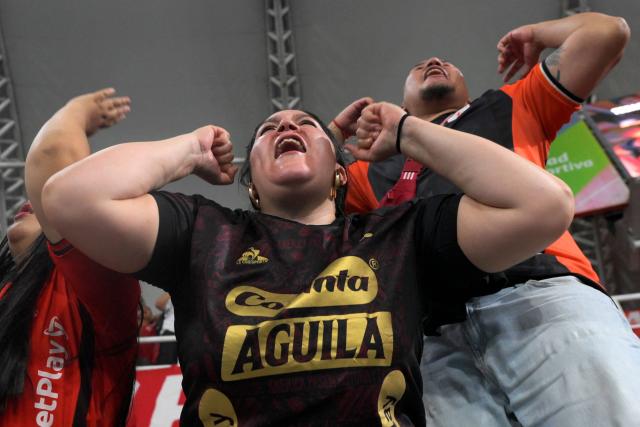 An America de Cali's fan from the Colectivo Futbolero Escarlata cheers for her team during the Copa Sudamericana football match between Colombia's America de Cali and Atletico Bucaramanga at the Olimpico Pascual Guerrero Stadium in Cali, Colombia on March 5, 2026. With a drum, a female fan sets the pace for the chants of a feminist fan club at the stadium in the Colombian city of Manizales. "One, two, three!" she says like an orchestra conductor surrounded exclusively by women tired of machismo in football, as is the case in other countries such as Brazil. (Photo by JOAQUIN SARMIENTO / AFP)