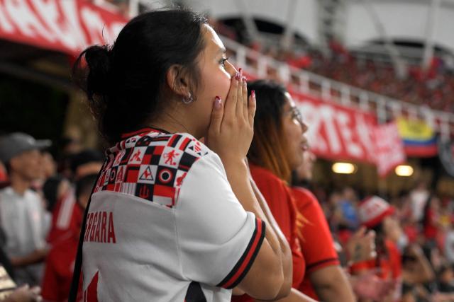 An America de Cali's fan from the Colectivo Futbolero Escarlata reacts during the Copa Sudamericana football match between Colombia's America de Cali and Atletico Bucaramanga at the Olimpico Pascual Guerrero Stadium in Cali, Colombia on March 5, 2026. With a drum, a female fan sets the pace for the chants of a feminist fan club at the stadium in the Colombian city of Manizales. "One, two, three!" she says like an orchestra conductor surrounded exclusively by women tired of machismo in football, as is the case in other countries such as Brazil. (Photo by JOAQUIN SARMIENTO / AFP)