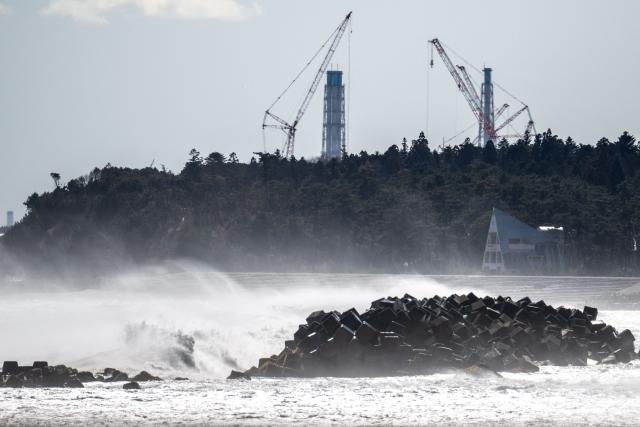 This picture taken on March 5, 2026 shows an abandoned building in front of the facilities of the Tokyo Electric Power Company's (TEPCO) Fukushima Daiichi Nuclear Power Plant (back), as seen from Ukedo fishing port in Namie, Fukushima prefecture. (Photo by Philip FONG / AFP)
