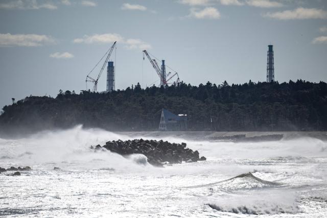 This picture taken on March 5, 2026 shows an abandoned building in front of the facilities of the Tokyo Electric Power Company's (TEPCO) Fukushima Daiichi Nuclear Power Plant (back), as seen from Ukedo fishing port in Namie, Fukushima prefecture. (Photo by Philip FONG / AFP)