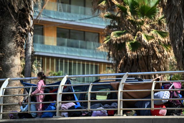 Displaced children who fled Israeli airstrikes in Beirut's southern suburbs stand next to belongings on the capital's corniche waterfront, where they took shelter, on March 6, 2026. Fresh strikes rocked Iran and Lebanon on March 6, as Israel vowed to escalate to a new phase in the Middle East war that has spiralled rapidly throughout the region and beyond. (Photo by Joseph EID / AFP)