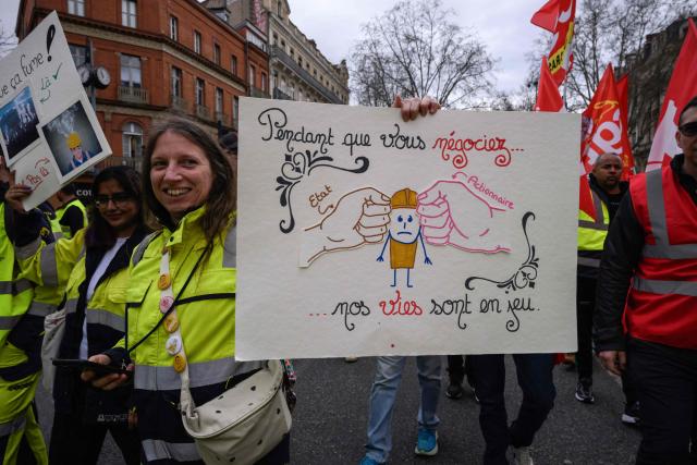 A protestor holds a placard reading "While you negotiate, our lives are in danger" during a demonstration by Fibre Excellence employees and unions as two factories in Saint-Gaudens and Tarascon are threatened with closure in Toulouse, southwestern France on March 6, 2026. (Photo by Ed JONES / AFP)