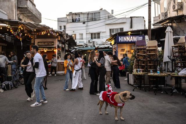Residents dance next to a dog outside a cafe along the street at Carmel market in Tel Aviv, on March 6, 2026. Israel's military on March 6 said that Iran had launched cluster bombs "multiple times" since the start of the war that began with a US-Israeli attack on the Islamic republic last week. (Photo by OLYMPIA DE MAISMONT / AFP)