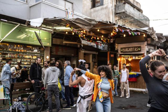 Residents dance outside a cafe along the street at Carmel market in Tel Aviv, on March 6, 2026. Israel's military on March 6 said that Iran had launched cluster bombs "multiple times" since the start of the war that began with a US-Israeli attack on the Islamic republic last week. (Photo by OLYMPIA DE MAISMONT / AFP)