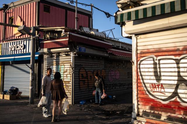 People carrying shopping bags walk past closed shops at Carmel market in Tel Aviv, on March 6, 2026. Israel's military on March 6 said that Iran had launched cluster bombs "multiple times" since the start of the war that began with a US-Israeli attack on the Islamic republic last week. (Photo by OLYMPIA DE MAISMONT / AFP)