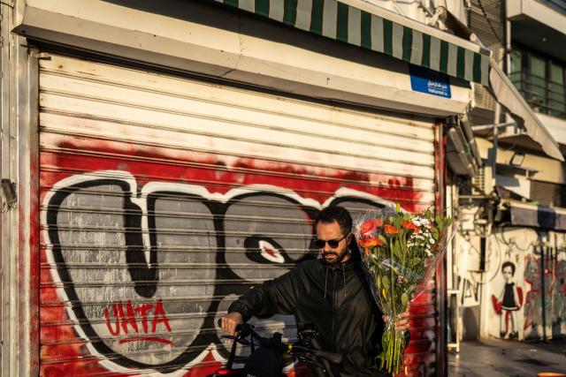 A man carries a flower bouquet as he pushes his bike past closed shops at Carmel market in Tel Aviv, on March 6, 2026. Israel's military on March 6 said that Iran had launched cluster bombs "multiple times" since the start of the war that began with a US-Israeli attack on the Islamic republic last week. (Photo by OLYMPIA DE MAISMONT / AFP)