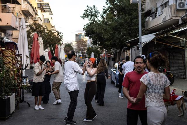TOPSHOT - Residents dance outside a cafe along the street at Carmel market in Tel Aviv, on March 6, 2026. Israel's military on March 6 said that Iran had launched cluster bombs "multiple times" since the start of the war that began with a US-Israeli attack on the Islamic republic last week. (Photo by OLYMPIA DE MAISMONT / AFP)