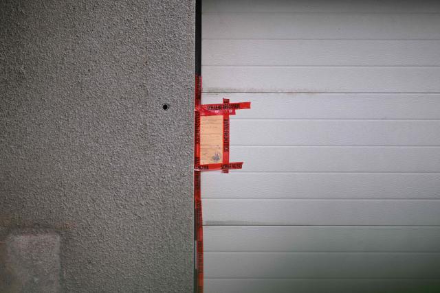 TOPSHOT - This photograph shows Police tape on a sealed garage door at the home of Liliane Coinchelin's youngest son suspected to have held his mother captive for several months leading to her death in Saint-Michel-sur-Meurthe, eastern France on March 6, 2026. A 39-year-old man has been charged with torture and barbaric acts resulting in the death of his mother, who died at least three years ago, the public prosecutor in Epinal, in the Vosges region, announced on March 6, 2026. The deceased woman's eldest son, aged 45, and his partner, aged 40, have been charged with complicity in acts of torture and barbarity resulting in death, unlawful confinement by an organised gang, and organised fraud. An investigation into her disappearance was launched after the mayor of Saint-Michel-sur-Meurthe reported on January 28, 2026 that Liliane Coinchelin, a resident of this village of some 1,700 inhabitants near Saint-Die-des-Vosges, had been missing for at least three years. (Photo by SEBASTIEN BOZON / AFP)