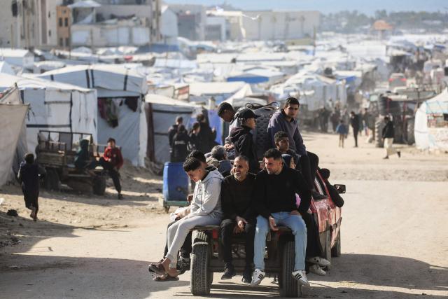 Palestinians ride in the back of a pick-up truck pas hundreds of tents are set up to house displaced Palestinians who lost their homes and businesses during Israeli military bombardment of the Gaza Strip, in Khan Yunis, in the south of the Gaza Strip on March 6, 2026. The majority of Gaza's 2.4 million people have been displaced, often multiple times, by the war that began with Hamas's attack on southern Israel on October 7, 2023. With displaced families living in tented camps, with serious concerns raised over their living conditions. (Photo by Bashar Taleb / AFP)