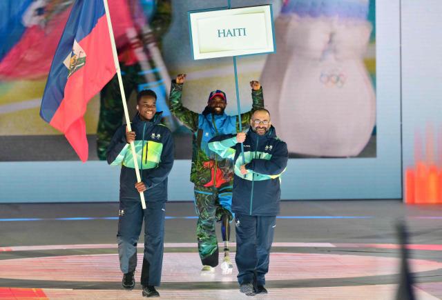 An athlete from Haiti (C) takes part in the delegation parade  as volunteers hold a nation flag and placard during the Milano Cortina 2026 Winter Paralympic Games opening ceremony at Arena di Verona in Verona on March 6, 2026. (Photo by Stefano RELLANDINI / AFP)