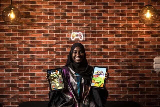 Game designer Mame Faty Kane poses for a portrait holding two of the video games she has created at the Game Hub in Dakar, on March 6, 2026. Mame Faty started playing video games at a young age. Instead of asking for dolls like her friends, she received a Game Boy from her parents. What began as a pastime slowly turned into a passion, and after finishing her studies, she began building her skills at Dakar’s Game Hub to become a game designer. To this day, she has created several video games, focusing mostly on educational ones like Cax Caxett (“find the riddle” in Wolof), where players can learn about Senegalese culture.“I can make my dreams come true when I create a video game. I’m always wondering, ‘Can I do this?’ and then I realize that there are no limits to what I can do as a game designer.” (Photo by PATRICK MEINHARDT / AFP)