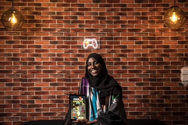Game designer Mame Faty Kane poses for a portrait holding one of the video games she has created at the Game Hub in Dakar, on March 6, 2026. Mame Faty started playing video games at a young age. Instead of asking for dolls like her friends, she received a Game Boy from her parents. What began as a pastime slowly turned into a passion, and after finishing her studies, she began building her skills at Dakar’s Game Hub to become a game designer. To this day, she has created several video games, focusing mostly on educational ones like Cax Caxett (“find the riddle” in Wolof), where players can learn about Senegalese culture.“I can make my dreams come true when I create a video game. I’m always wondering, ‘Can I do this?’ and then I realize that there are no limits to what I can do as a game designer.” (Photo by PATRICK MEINHARDT / AFP)