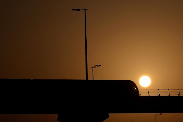 A metro train is silhouetted against the rising sun in Doha on March 7, 2026. (Photo by Karim JAAFAR / AFP)