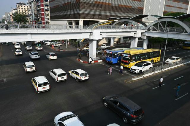 Vehicles and pedestrians cross an intersection on the first day of the implementation of an "odd-even" vehicle numbering system in Yangon on March 7, 2026. Myanmar's junta announced half of private vehicles will be ordered off the roads each day, based on licence plate numbers, in order to conserve fuel due to the war in the Middle East. Myanmar imports 90 percent of its fuel oil, according to 2024 figures, and has long suffered from a fragile energy supply chain owing to the civil war consuming the country since the military staged a coup five years ago. (Photo by Sai Aung MAIN / AFP)