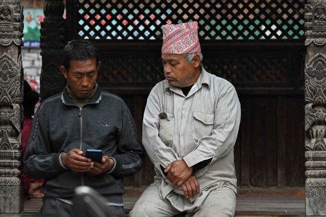 People check election results on a mobile phone at Durbar Square in Bhaktapur near Kathmandu on March 7, 2026. Nepal's centrist party of rapper-turned-politician Balendra Shah looked set to win by a landslide in parliamentary polls, according to Election Commission trends March 7, but with counting still far to go. (Photo by Tauseef MUSTAFA / AFP)