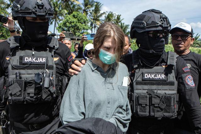 Russian national suspects Natalia (C), 30, accused of operating a laboratory producing the synthetic drug mephedrone, is escorted by police to the house used to manufacture drugs during a crime scene reconstruction as authorities search for another foreign suspect in Gianyar, on Indonesia's resort island of Bali on March 7, 2026. (Photo by LANA PRIATNA / AFP)