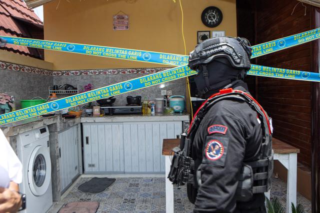 A police officer secures a crime scene as Russian national suspects  S.T. (not pictured) and Natalia (not pictured), both accused of operating a laboratory producing the synthetic drug mephedrone, are brought to the house used to manufacture drugs during a crime scene reconstruction as authorities search for another foreign suspect in Gianyar, on Indonesia's resort island of Bali on March 7, 2026. (Photo by LANA PRIATNA / AFP)