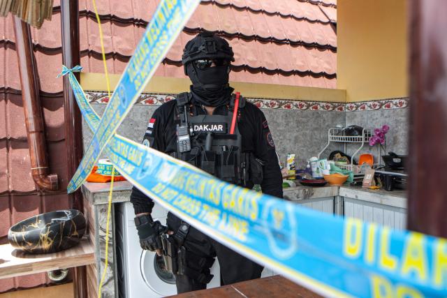 A police officer secures a crime scene as Russian national suspects  S.T. (not pictured) and Natalia (not pictured), both accused of operating a laboratory producing the synthetic drug mephedrone, are brought to the house used to manufacture drugs during a crime scene reconstruction as authorities search for another foreign suspect in Gianyar, on Indonesia's resort island of Bali on March 7, 2026. (Photo by LANA PRIATNA / AFP)