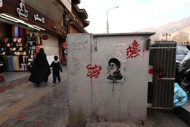 An Iranian woman holds a hand of a boy as they walks past a shop and an image of Iran's slain supreme leader Ayatollah Ali Khamenei (R), along a street at the Tajrish Square in Tehran on March 7, 2026. Iran's army said Saturday its navy had launched a wave of drone attacks targeting Israel as well as US bases in the United Arab Emirates and Kuwait, as the regional war raged into its second week. (Photo by ATTA KENARE / AFP)