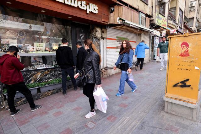 Iranian women walks past a watch shop and an image of Iran's slain supreme leader Ayatollah Ali Khamenei (R), along a street at the Tajrish Square in Tehran on March 7, 2026. Iran's army said Saturday its navy had launched a wave of drone attacks targeting Israel as well as US bases in the United Arab Emirates and Kuwait, as the regional war raged into its second week. (Photo by ATTA KENARE / AFP)