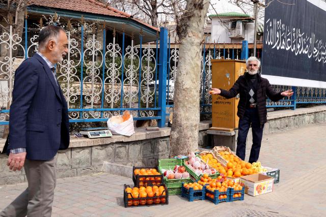 Iranian man walks past a fruit vendor set up near Tajrish Square in Tehran on March 7, 2026. Iran's army said Saturday its navy had launched a wave of drone attacks targeting Israel as well as US bases in the United Arab Emirates and Kuwait, as the regional war raged into its second week. (Photo by ATTA KENARE / AFP)