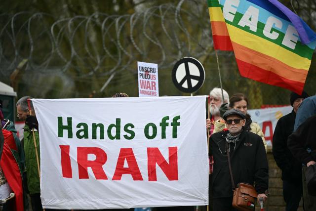 Anti-war protesters gather with banners at an entrance to RAF Fairford in south west England shortly after sunrise on March 7, 2026. Britain's Prime Minister Keir Starmer has given approval for Washington to use the bases of Diego Garcia in the Indian Ocean and RAF Fairford in south-west England to bomb Iranian missile sites, after several Gulf countries were targeted by Iranian retaliations. (Photo by JUSTIN TALLIS / AFP)
