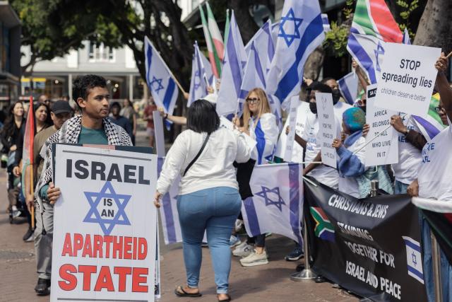 TOPSHOT - A pro Palestinian supporter holds a placard during a counter demonstration while supporters of Israel and Iranian pro-democracy activists hold a rally in on one of the main alley of the Victoria and Albert Waterfront shopping mall in Cape Town, on March 7, 2026. (Photo by GIANLUIGI GUERCIA / AFP)